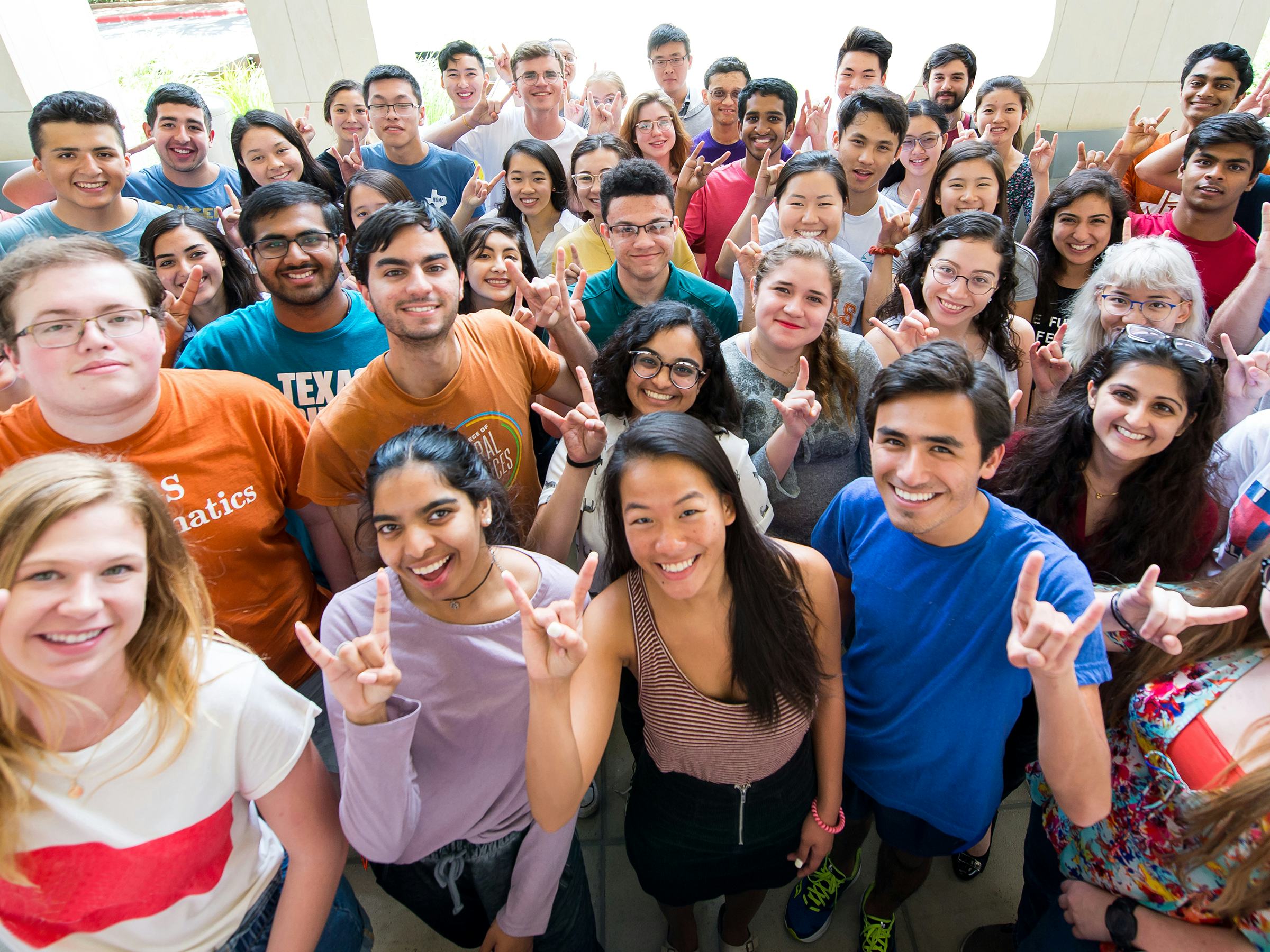 Large group of science students on the NHB patio smiling with Hook 'em hand gestures.
