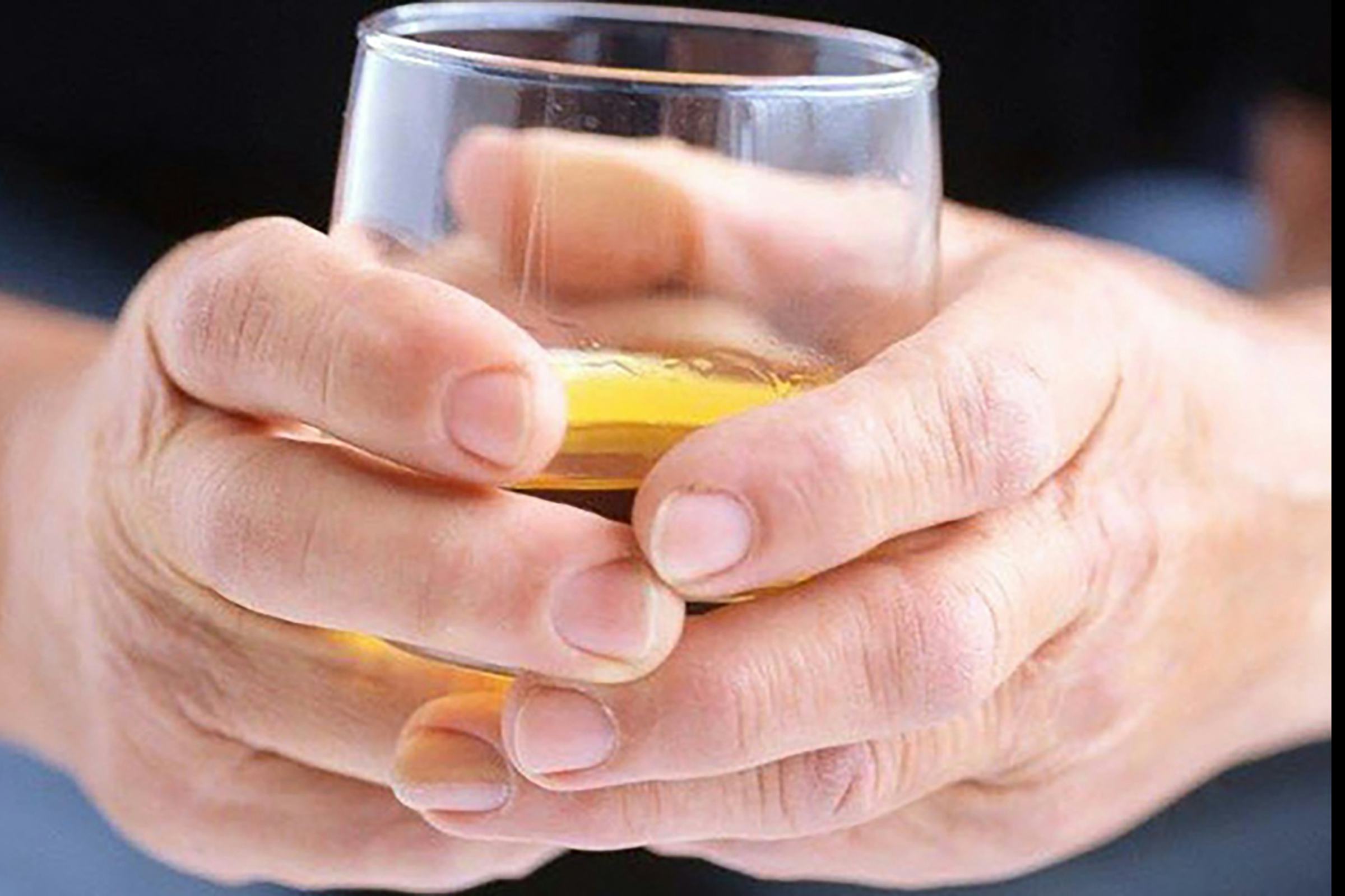 A pair of hands holding a glass of semi-clear yellowish liquid