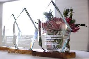 Glass awards on a white table in front of a floral arrangement 
