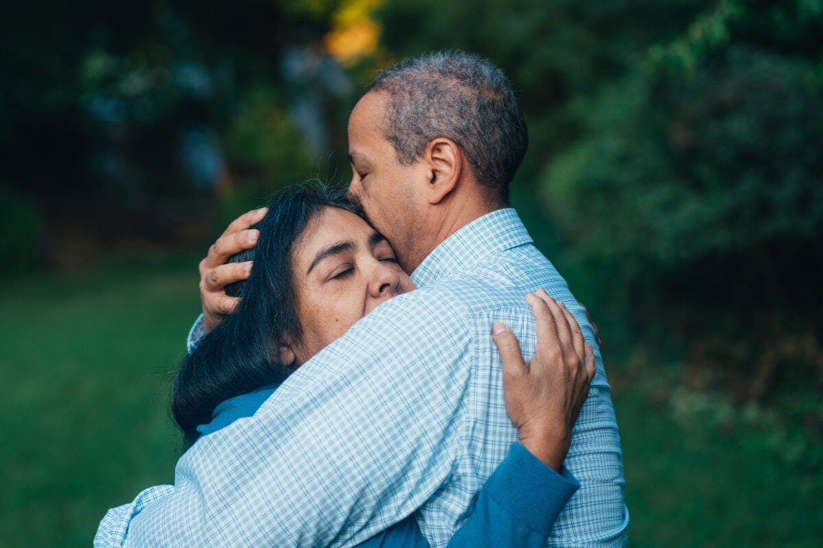 A Hispanic woman, left, is hugged by a man in a blue shirt on the right