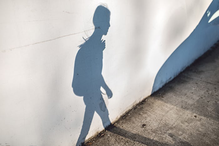 Shadow of a young person wearing a backpack on a white wall