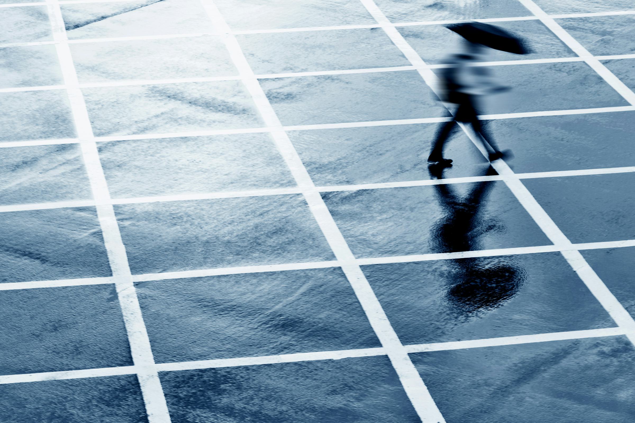 A person with an umbrella walks across a grid of intersecting white lines