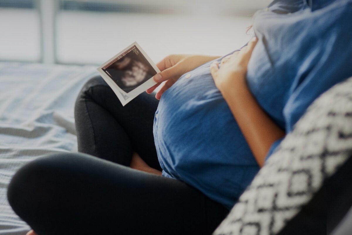 Photo of a pregnant woman seated as she looks at an ultrasound photo