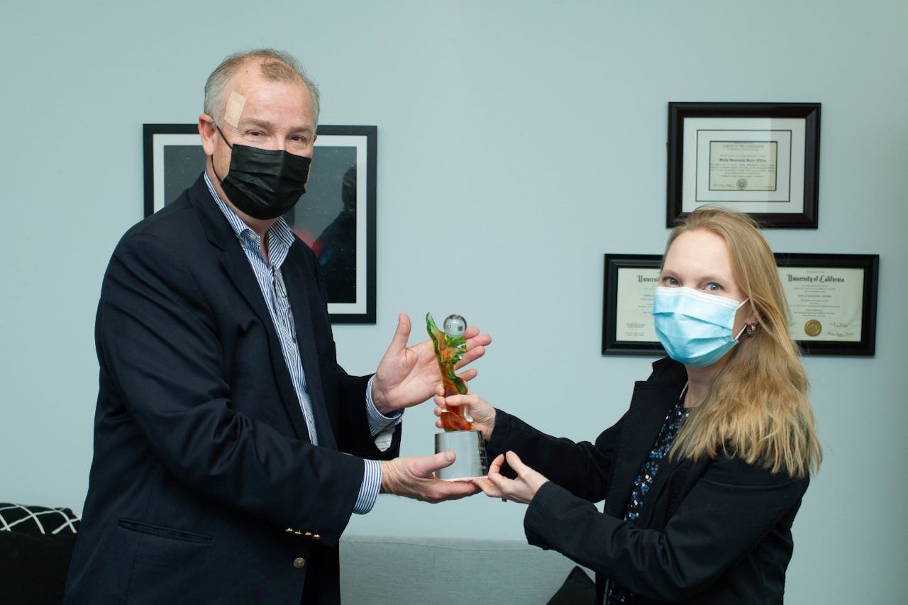 A man in a face mask presents a statuette to a woman in a face mask
