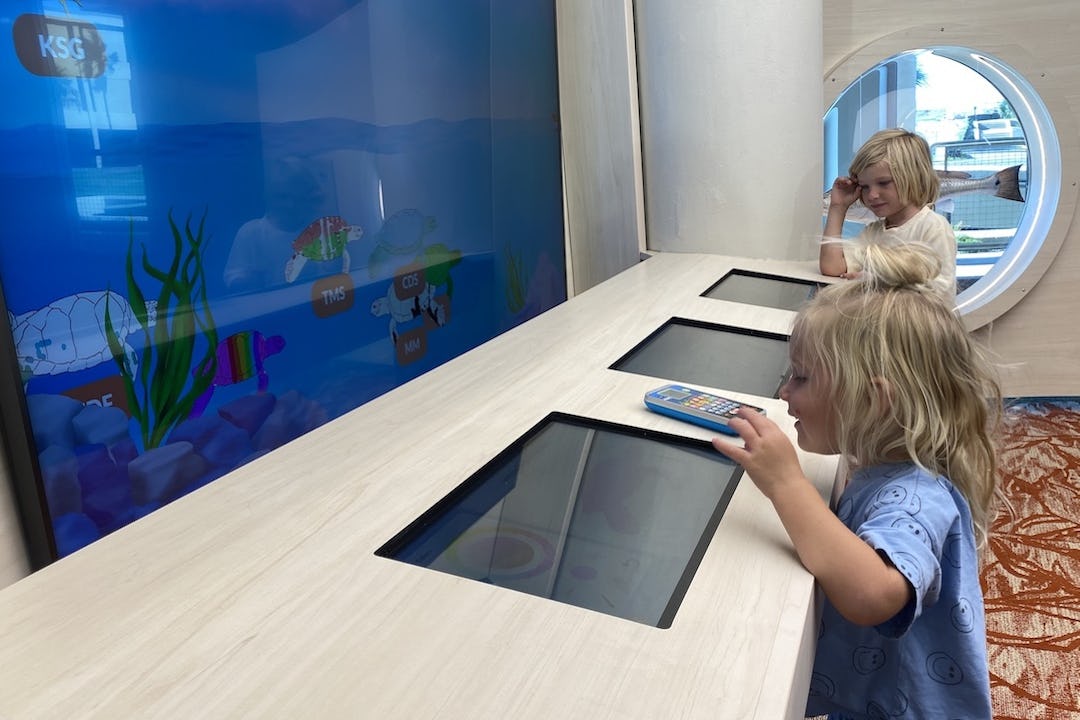 Two young children play at an exhibit that shows underwater sea life on a screen