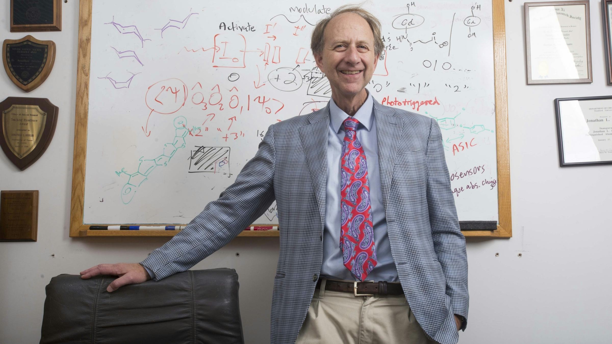 Jonathan Sessler, in suit and tie, smiles and stands before white board with notes