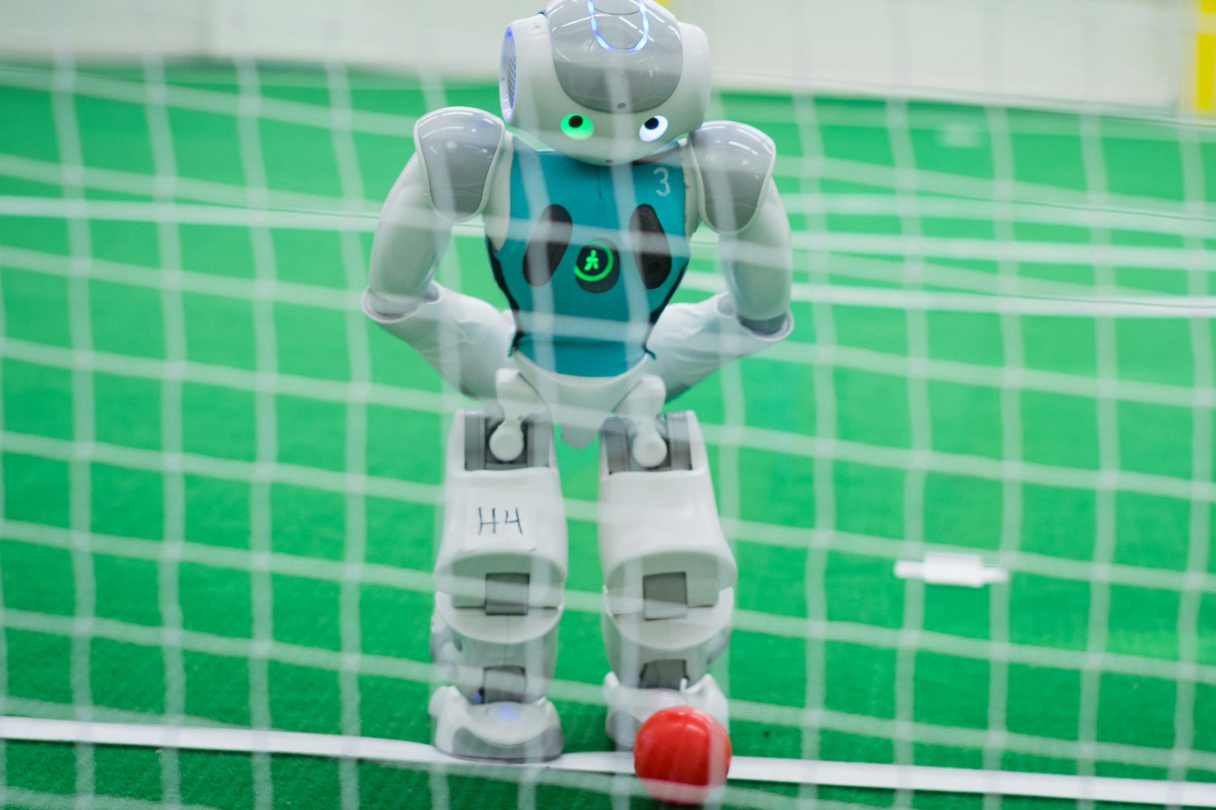 Robot standing on a soccer pitch preparing to kick a red ball into a net