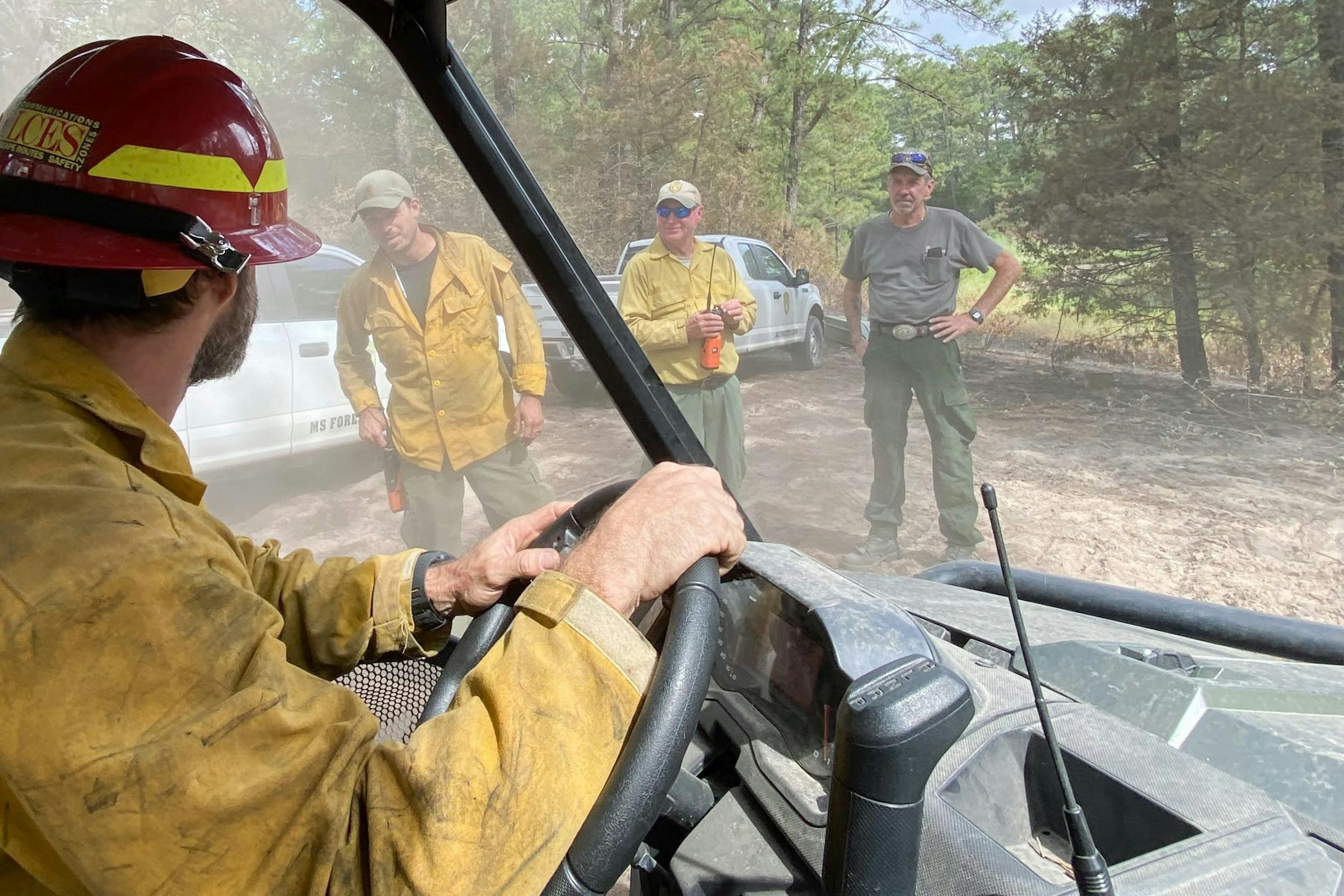 Firefighter at wheel of vehicle consults with colleagues outdoors
