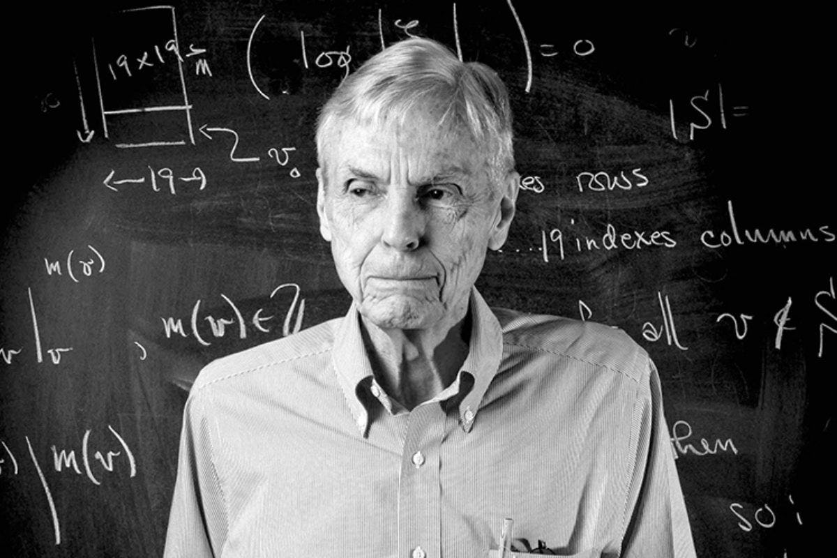Mathematician John Tate in front of a blackboard with equations