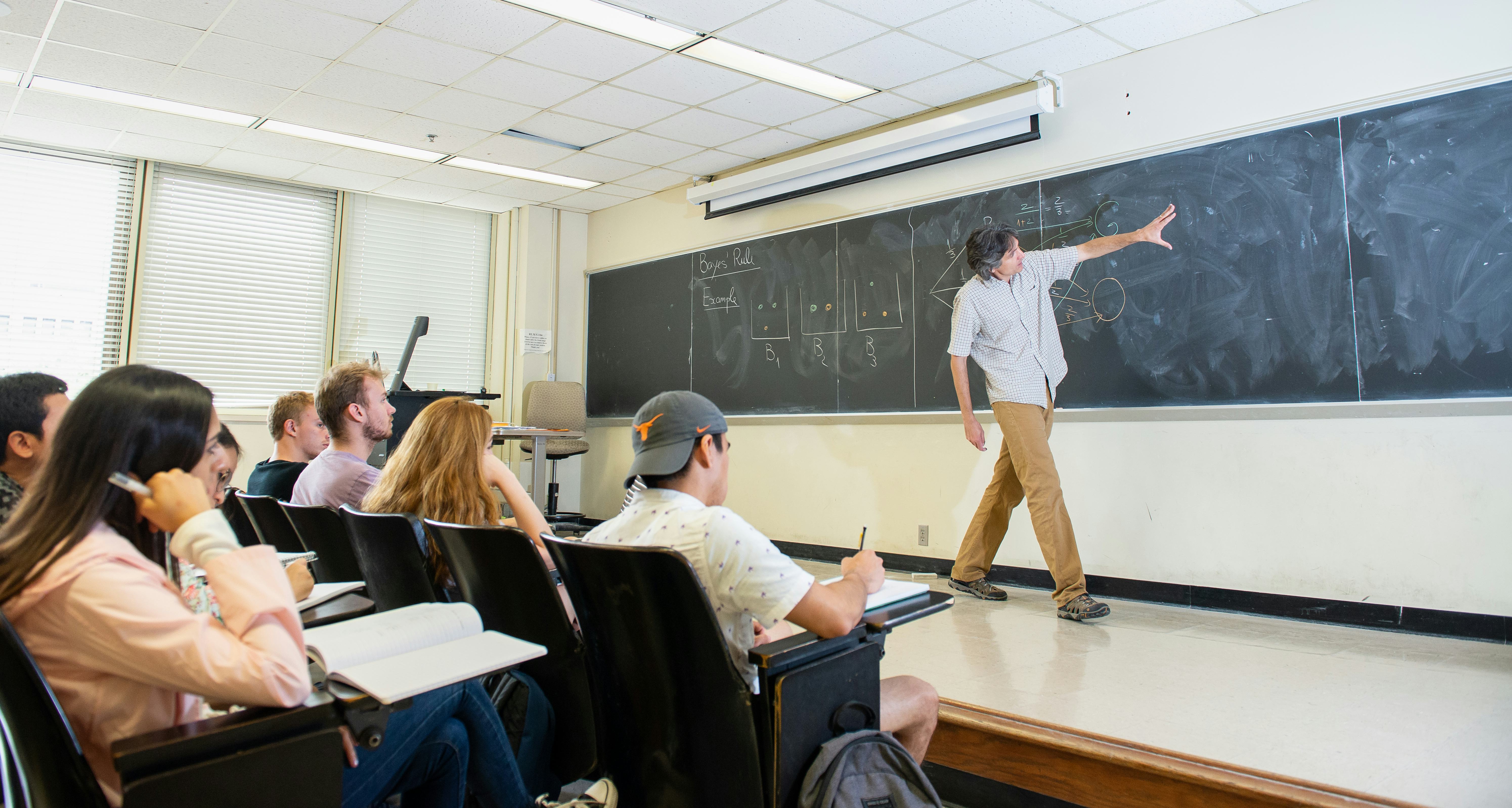Professor at chalk board with students in class