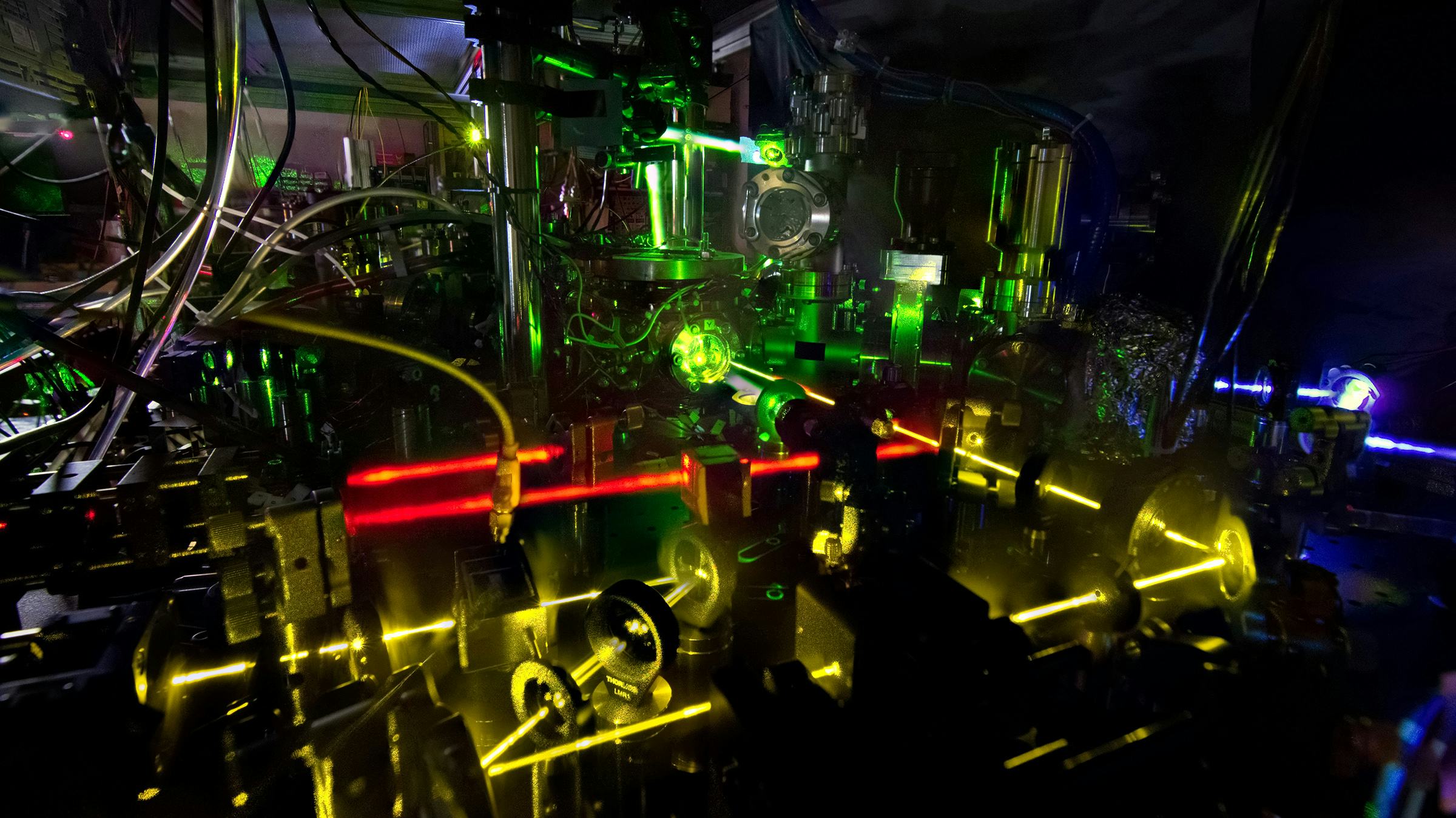 Glowing laser beams in red, yellow and green criss-cross an atomic clock